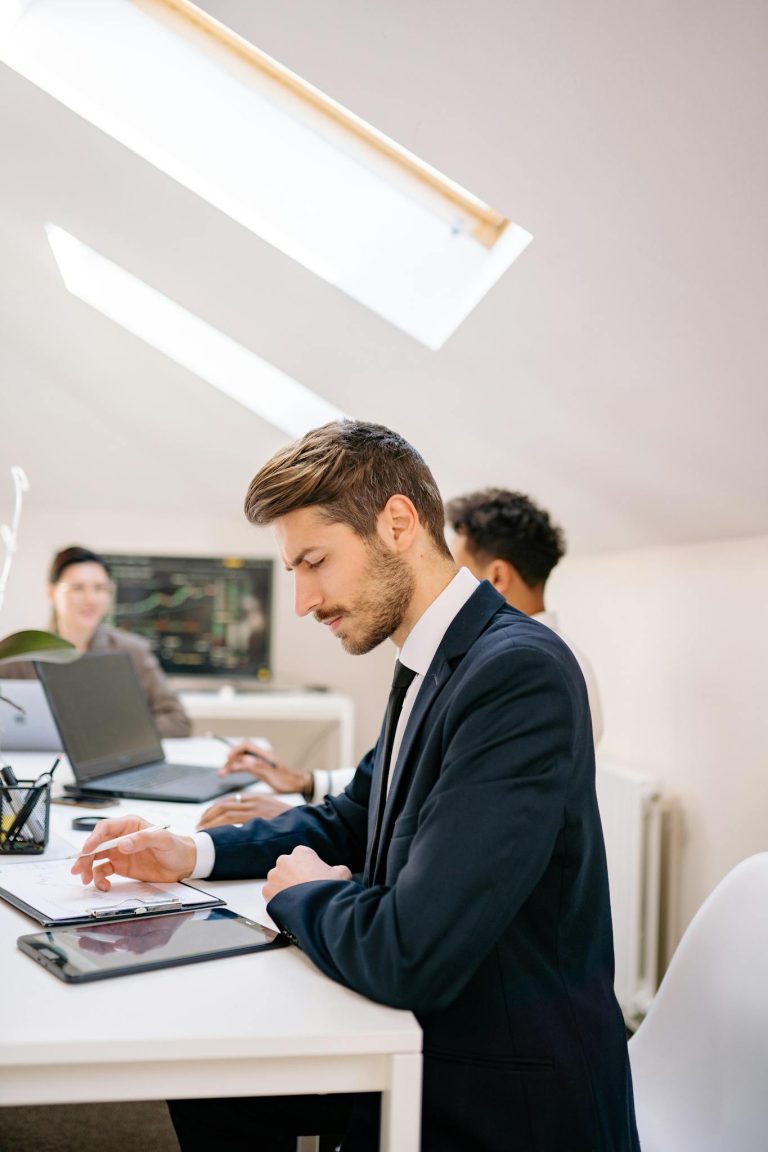 Business professionals in a modern office setting working on tablets and laptops, showcasing teamwork and productivity.
